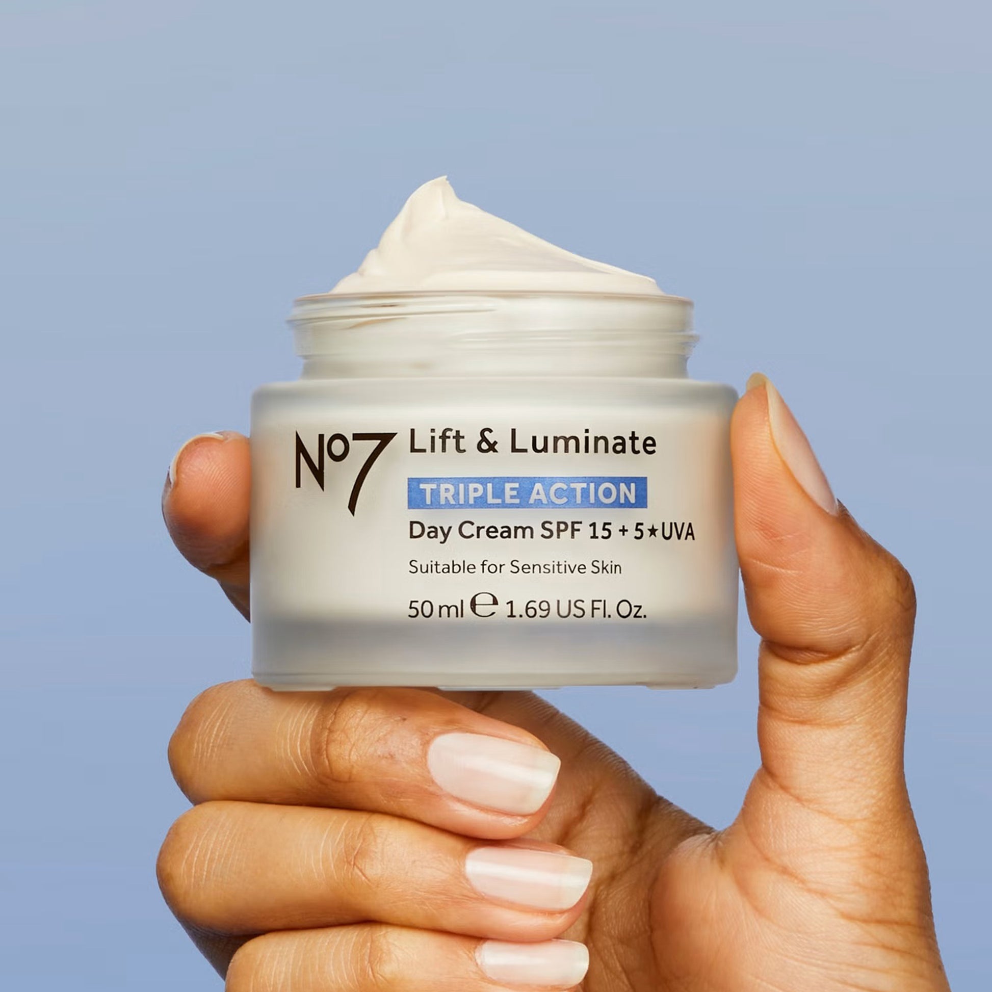 Hand holding a jar of No7 Lift & Luminate day cream against a blue background