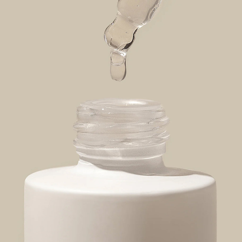 Close-up of a dropper bottle with liquid being dispensed onto a beige background