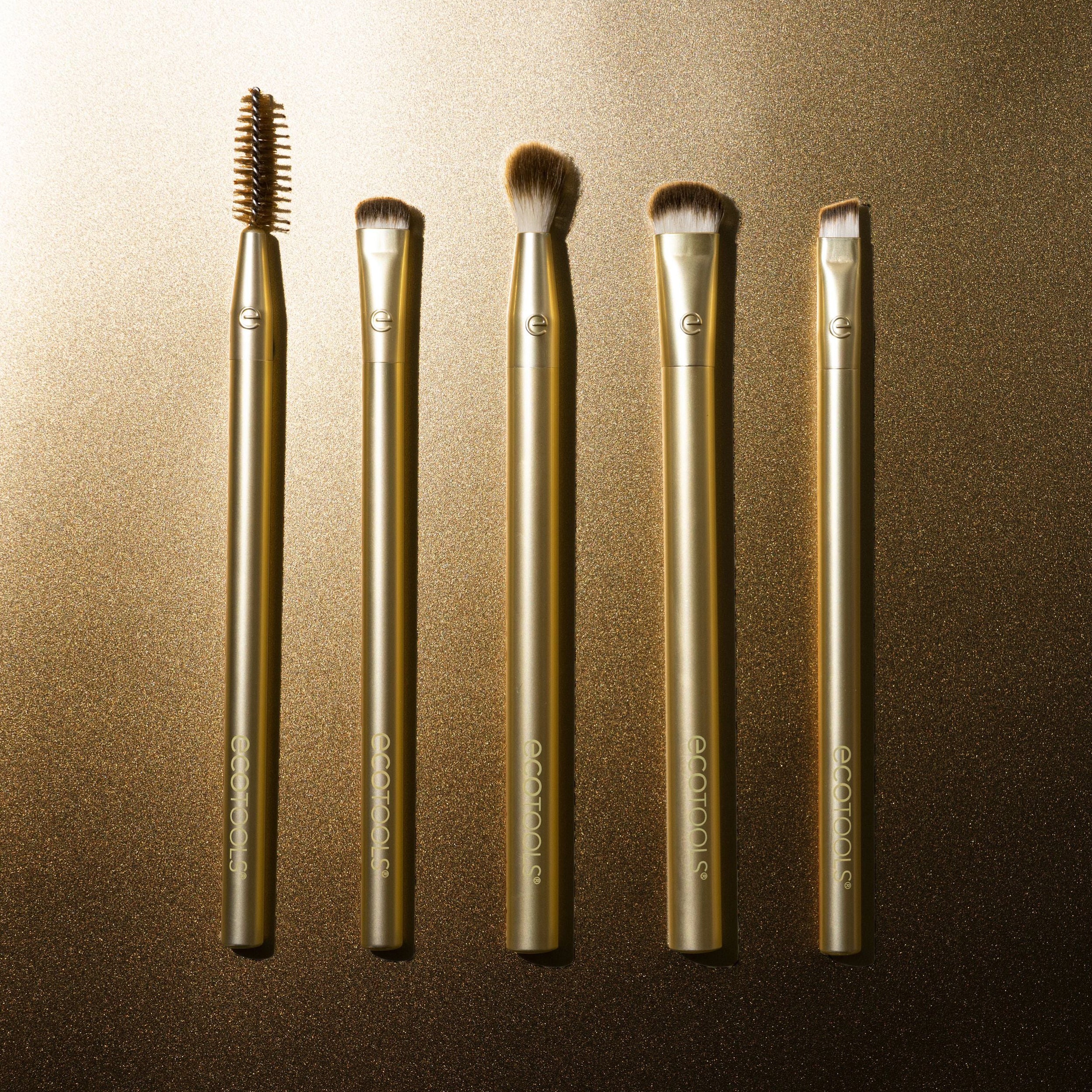 Set of five gold makeup brushes on a brown background