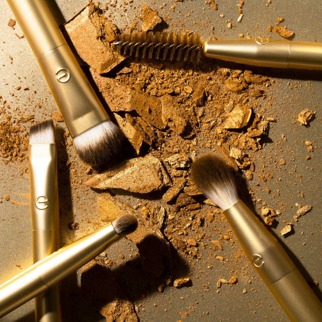 Makeup brushes with gold handles on a textured surface with makeup powder.