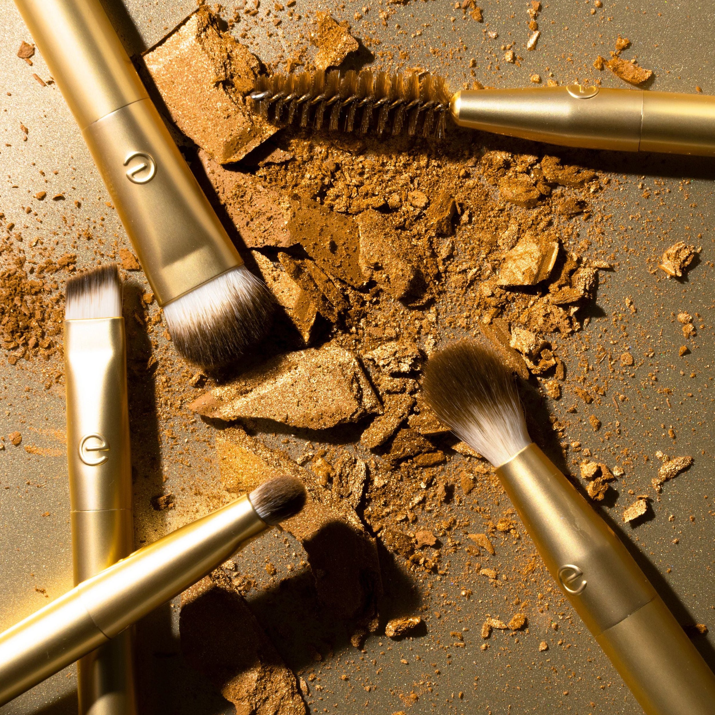 Makeup brushes with gold handles on a textured surface with makeup powder.