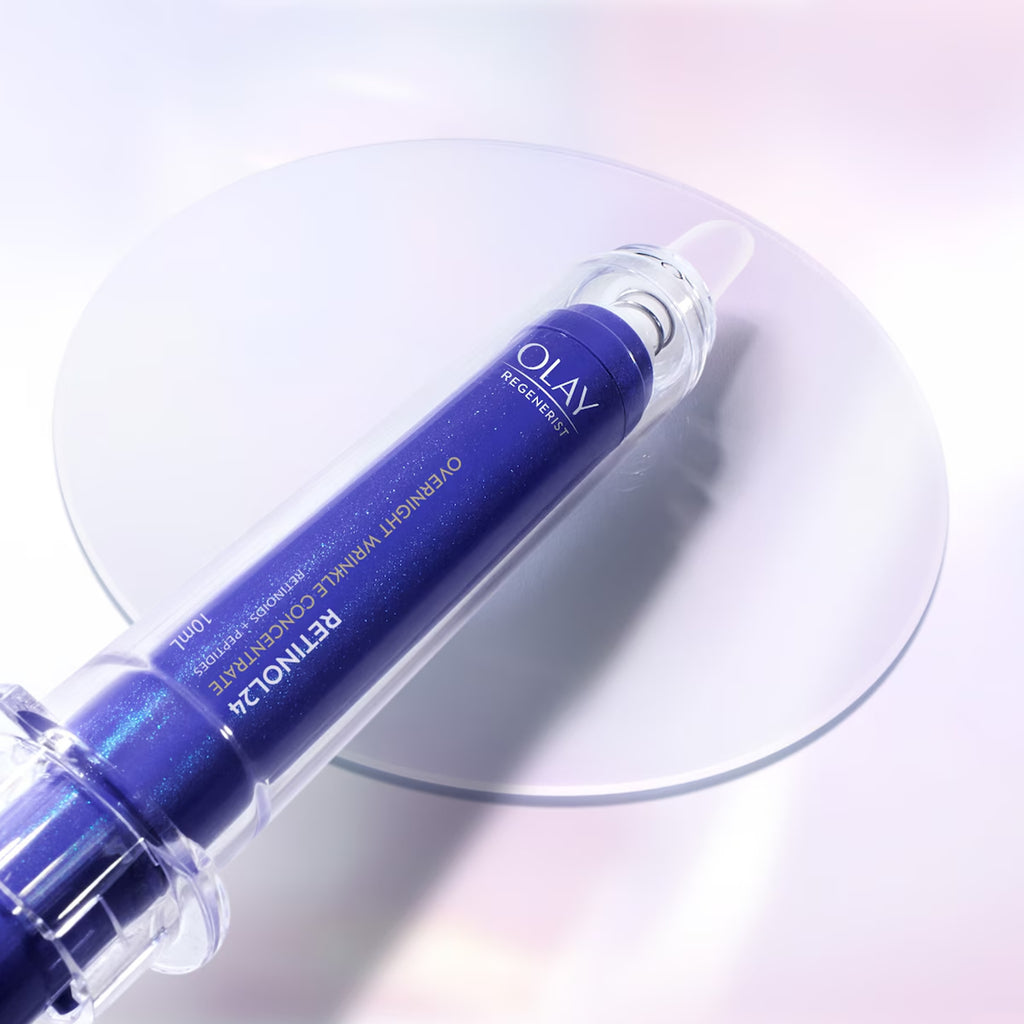 Olay Retinol 24% Overnight Wrinkle Concentrate in a deep blue cylindrical bottle with a clear cap, resting diagonally on a reflective circular glass plate against a soft white and pink gradient background.