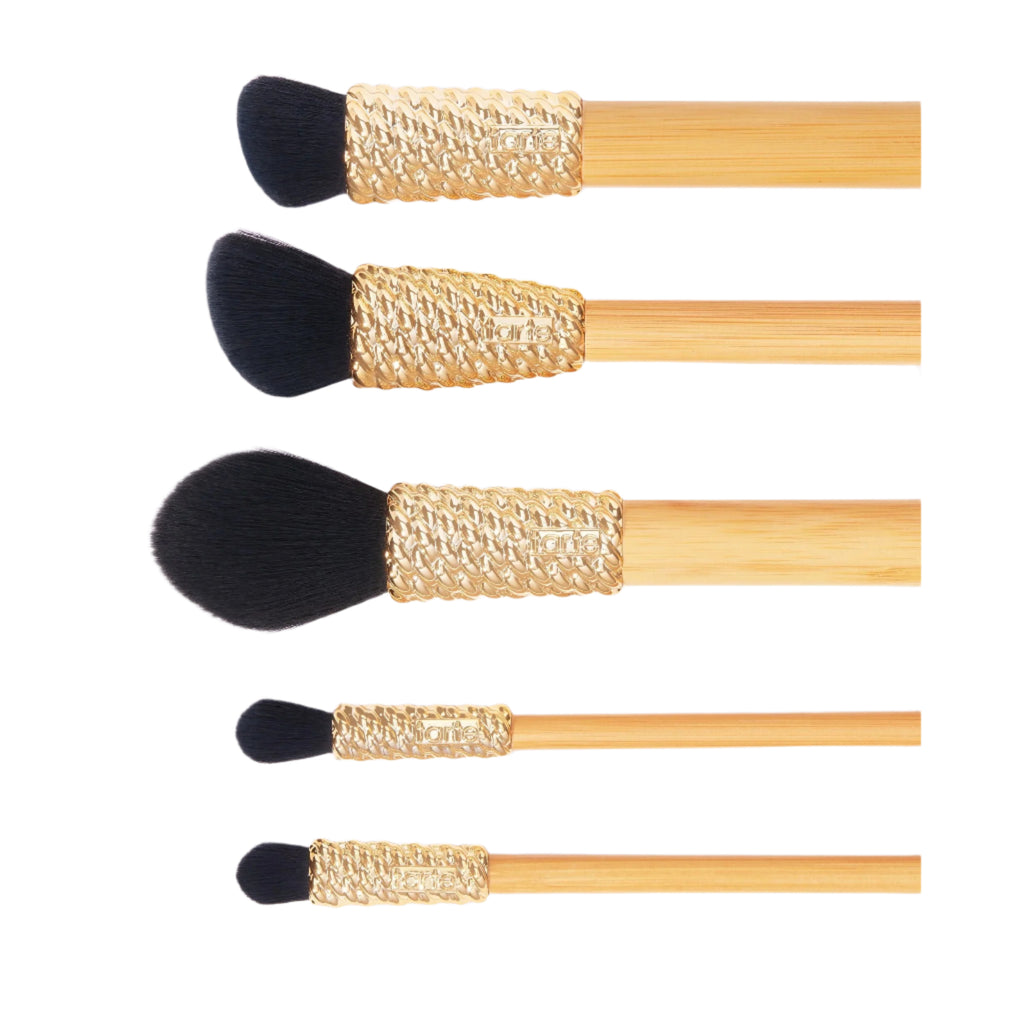 Set of five makeup brushes with gold ferrules and black bristles on a light purple background.