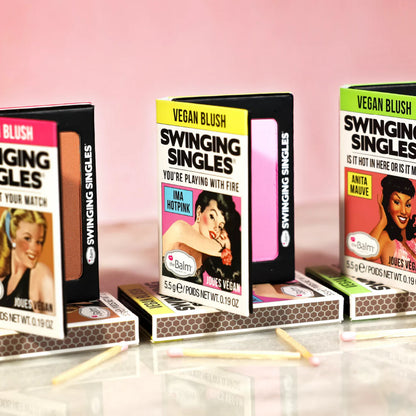 Three boxes of 'Swinging Singles' makeup products on a pink background